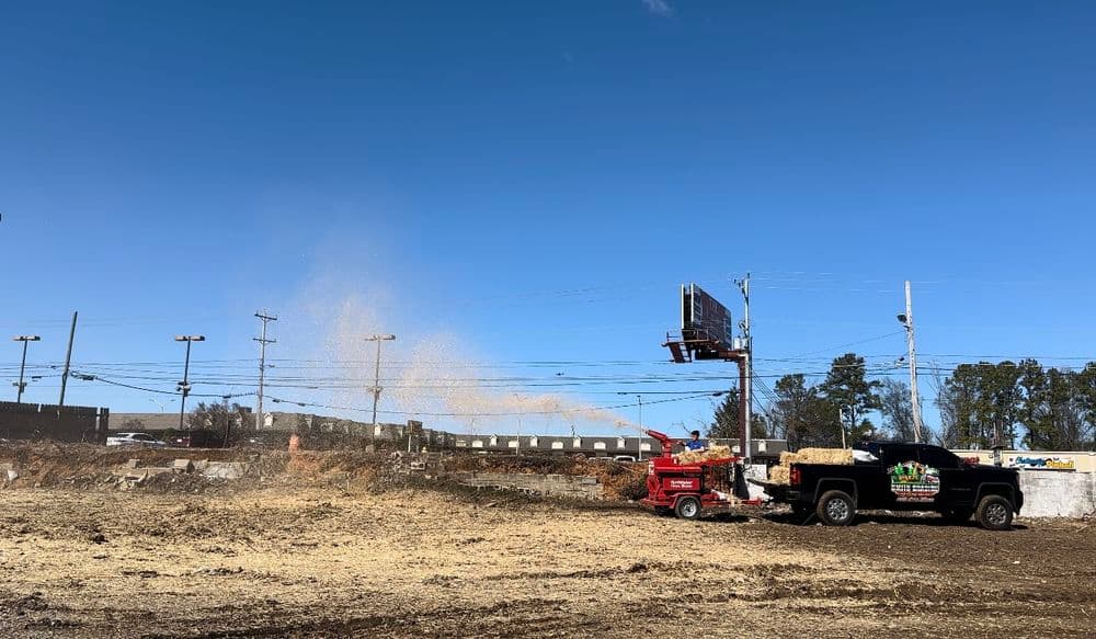 Chipper truck spraying wood chips on a construction site against a clear blue sky.