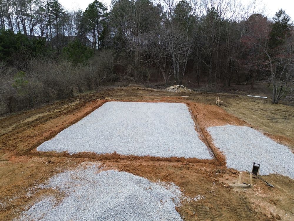 Gravel foundation prepared for construction on a cleared lot surrounded by trees.