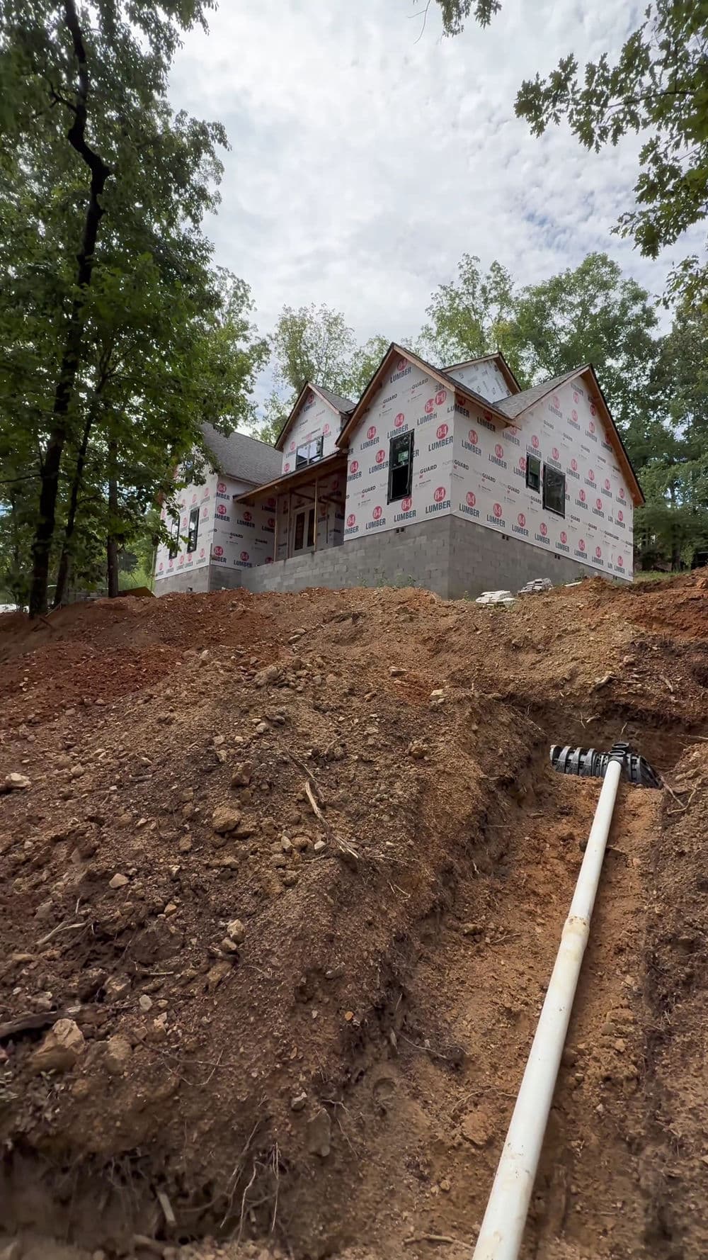 Newly constructed house with protective wrap, surrounded by trees and earth excavation.
