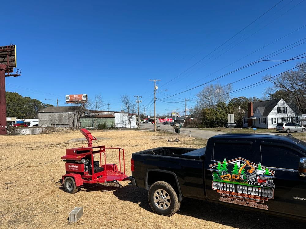 Truck with logo and wood chipper on cleared lot, blue sky, and billboard in background.