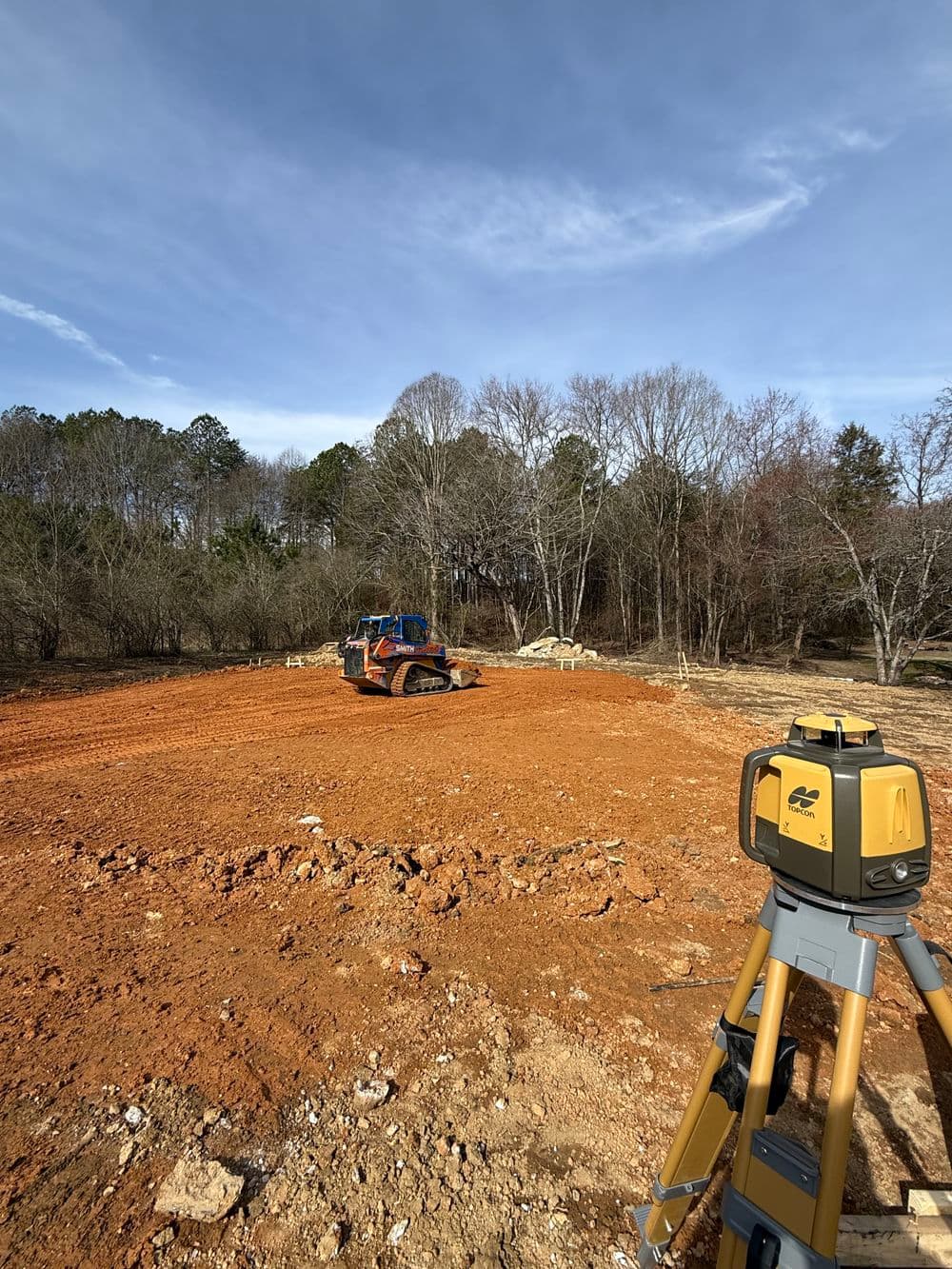Construction site with heavy machinery and surveying equipment on cleared land.