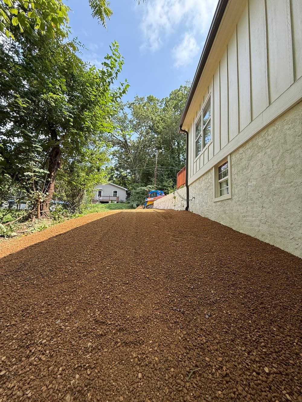 Gravel driveway leading to a house with trees and a playground in the background.
