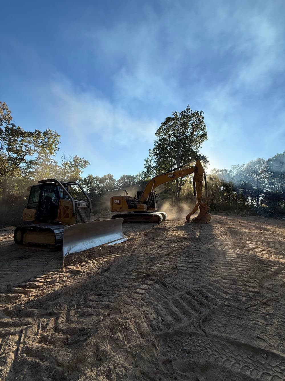 Excavators working on a construction site under a clear blue sky. Dust rises in the air.
