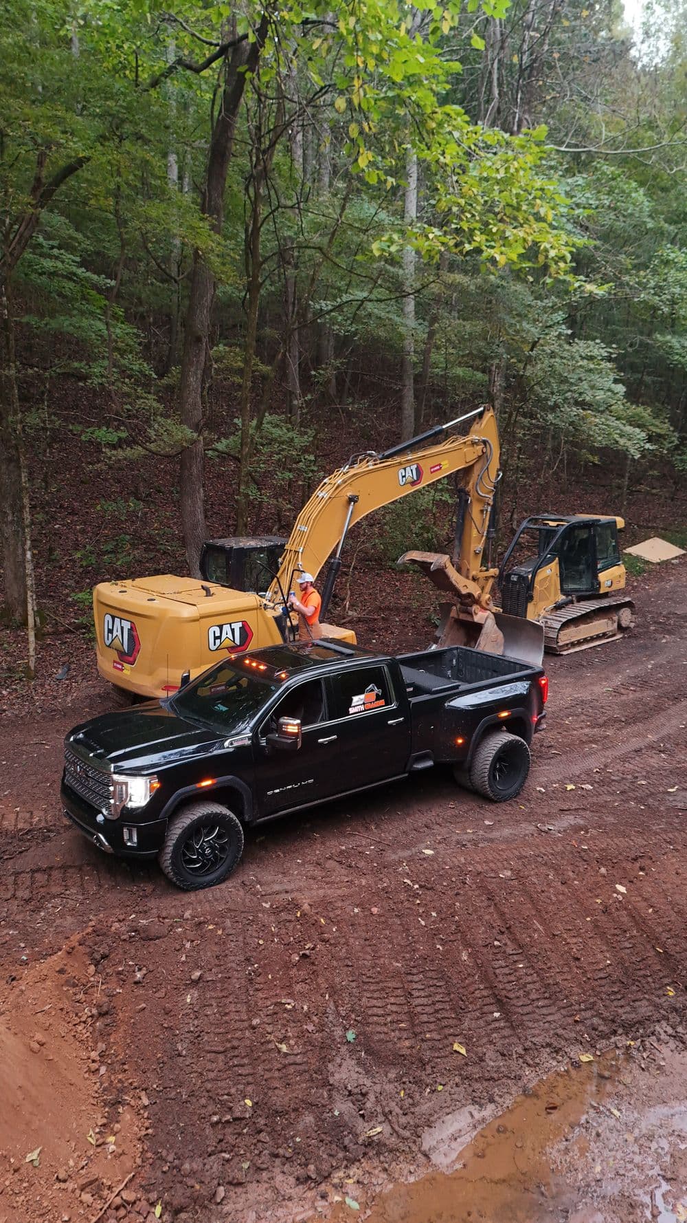 Black pickup truck and CAT machinery working on a forest construction site.
