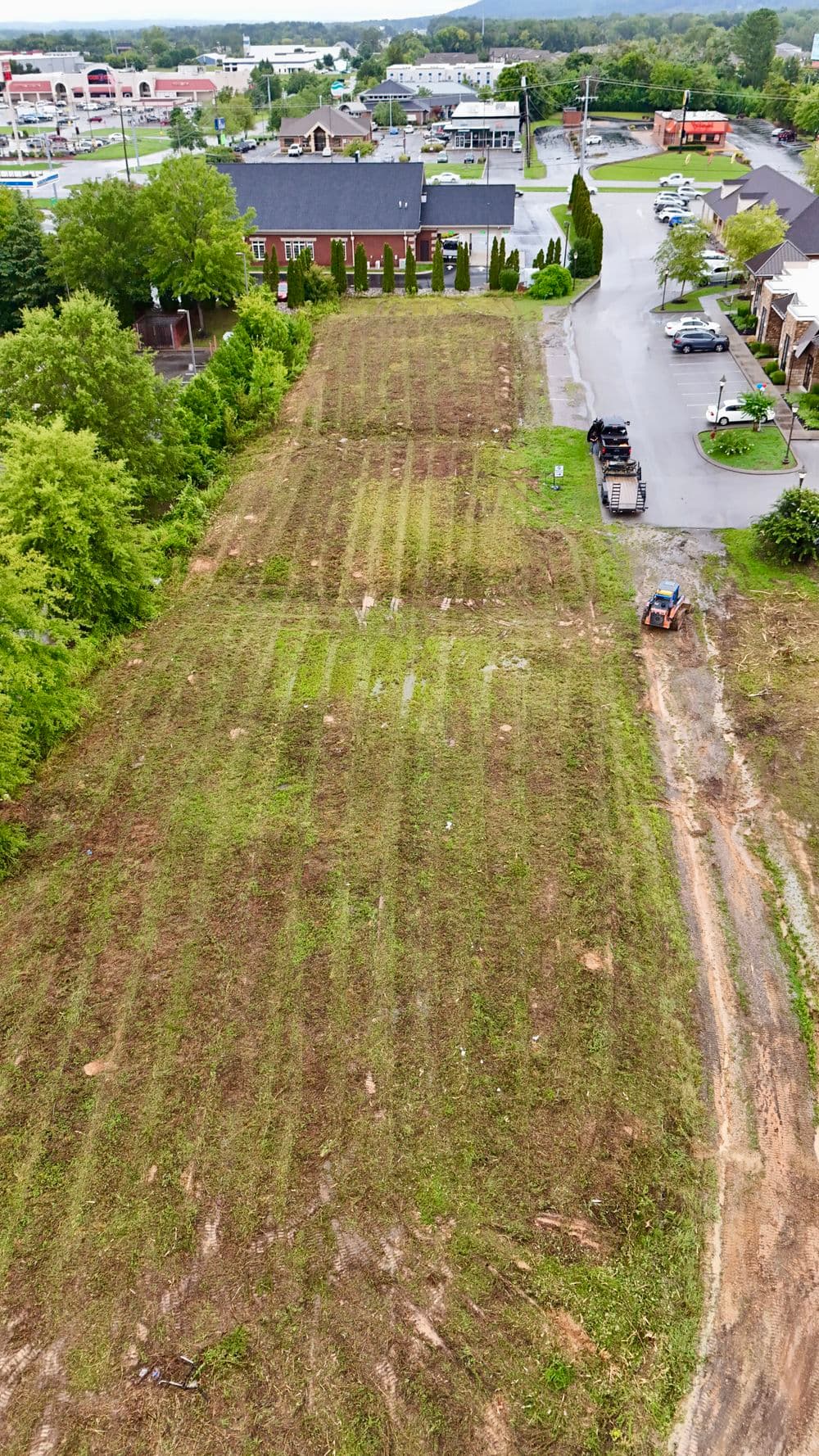 Aerial view of a cleared land with vegetation near commercial buildings and a road.